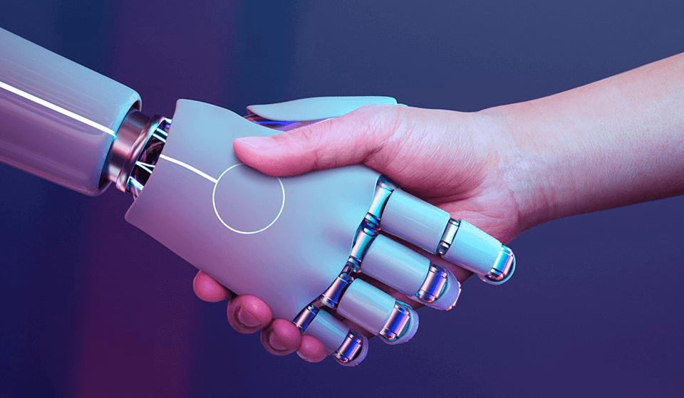 Uma mão de uma pessoa apertando a mão de um robô, para ilustrar a inteligência artificial.
